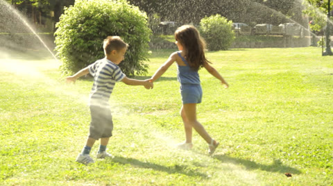 Kids are playing in a park with sprinklers.