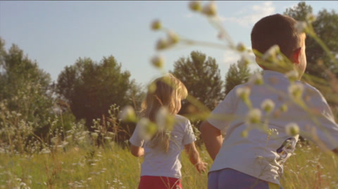 Two happy kids running on green field over sunset