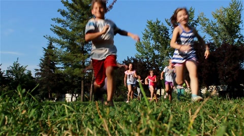 Children running in the park. Kids race on the green grass. Slow motion.