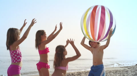 Slow motion of five children playing with beach ball on beach.