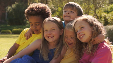 Group of five kids sitting on grass together in park.