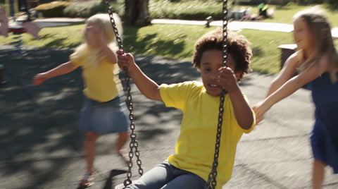 Four children playing on swings in park.