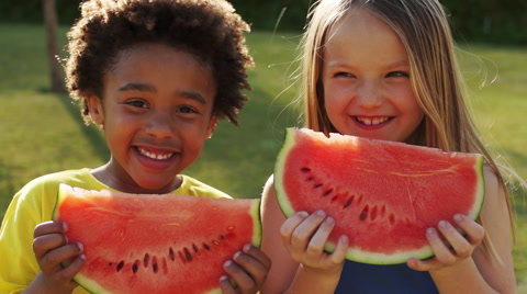 Two children eating water melon in park.