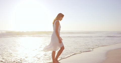 Beautiful woman wearing white dress walking on beach at sunset in slow motion