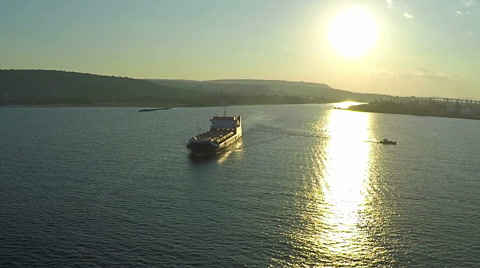 AERIAL, trade ship leaving the harbor at the sunset time going to open ocean.