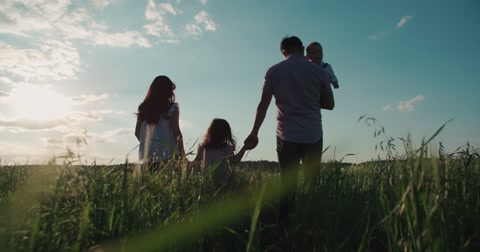 young happy Asian family goes on a green field with two children, slow motion