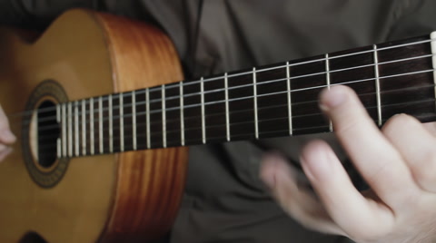 Man masterfully plays on classical acoustic guitar in the dark room close-up