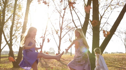 Young girls children kids playing running in fallen autumn leaves