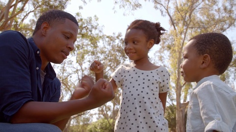 Mixed race man playing with his kids in the park, low angle