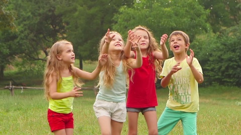 Happy children boy and three girls playing catch soap bubbles on a summer lawn