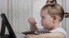 A little cute girl eats food and watches cartoons on the tablet. … [138117632] | 写真素材・ストックフォトのアフロ