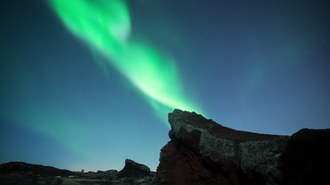 Aurora borealis swirling over moonlit jagged volcanic terrain Iceland pro res