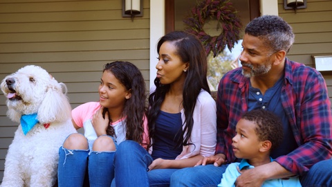 Family With Children And Pet Dog Sit On Steps Of Home