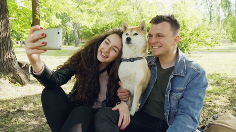 Proud dog owners happy couple are taking selfie with beautiful pet having fun