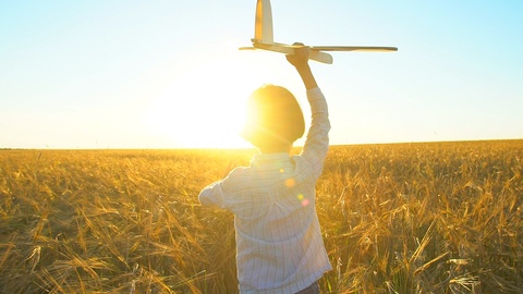 Happy little boy child running with toy airplane in wheat field at sunset. Kid