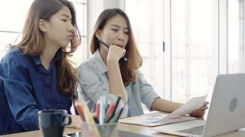 Asian business women working on laptop while sitting on desk in office.