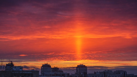 Light pillar atmospheric effect from sunset sun over epic red clouds, dark city