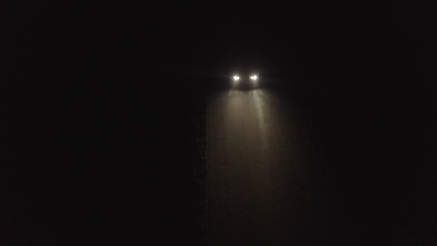 Aerial view tracking a car driving down a rural lane at night at speed.