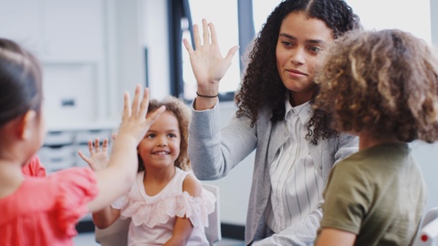 Infant school kids giving their teacher a high five in the classroom after