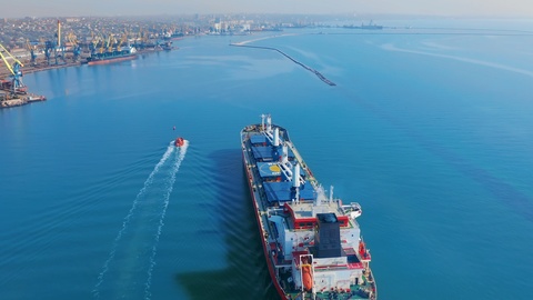 Aerial view. Large cargo ship enters the port city with port cranes.