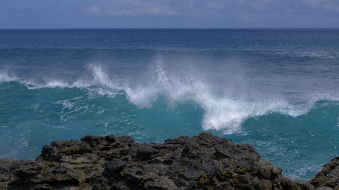 CLOSE UP: Big waves crash into the black volcanic rocks on the remote shore.