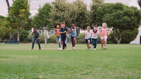 Group Of Excited Children Playing With Friends And Running Across Grass Playing