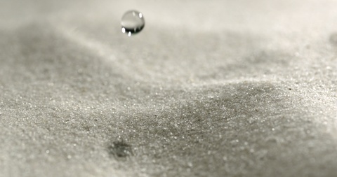 A drop of water is falling in slow motion on the sand.