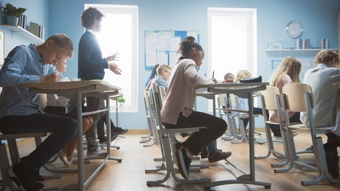 In Elementary School Class: Enthusiastic Teacher walks between Rows of Children