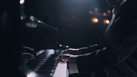 Male pianist playing classical piano on stage in a hall 