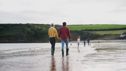 Rear View Of Family With Pet Dog Walking Along Beach Shoreline On Winter