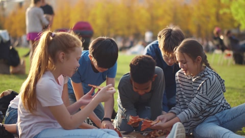 Group of happy multiethnic children eating pizza outdoors