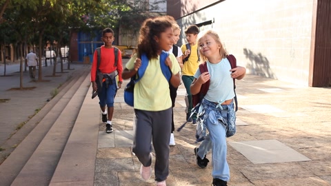 Group of children with backpacks walking on street near school