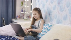 A little teenage girl uses a laptop while sitting on the bed. … [158331043] | 写真素材・ストックフォトのアフロ