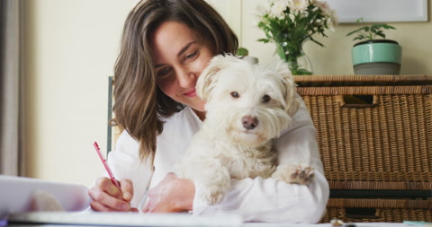 Caucasian woman drawing working from home and cuddling her pet dog