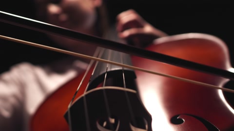 Musician leads bow along strings of cello playing classical music, closeup