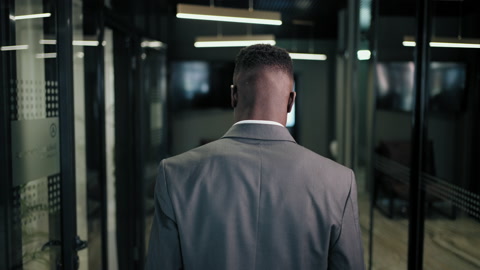 The camera follows the back of a man walking down the corridor of a business