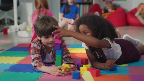 Cute multiethnic preschool kids playing with colored blocks on floor at nursery