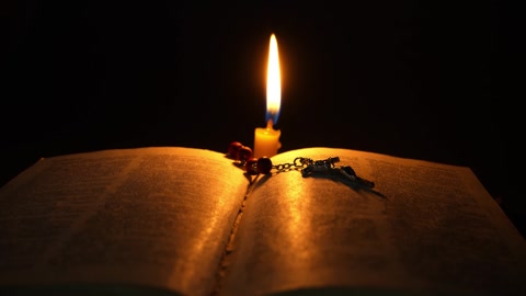 An open Bible in the dark in the light of a burning candle. …の動画素材